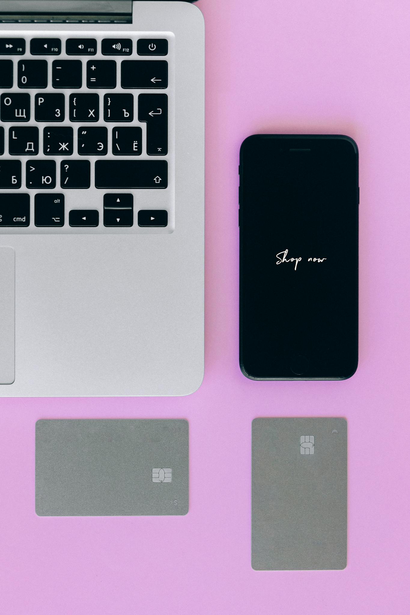 Flat lay of laptop, smartphone, and credit cards for online shopping on a pink background.